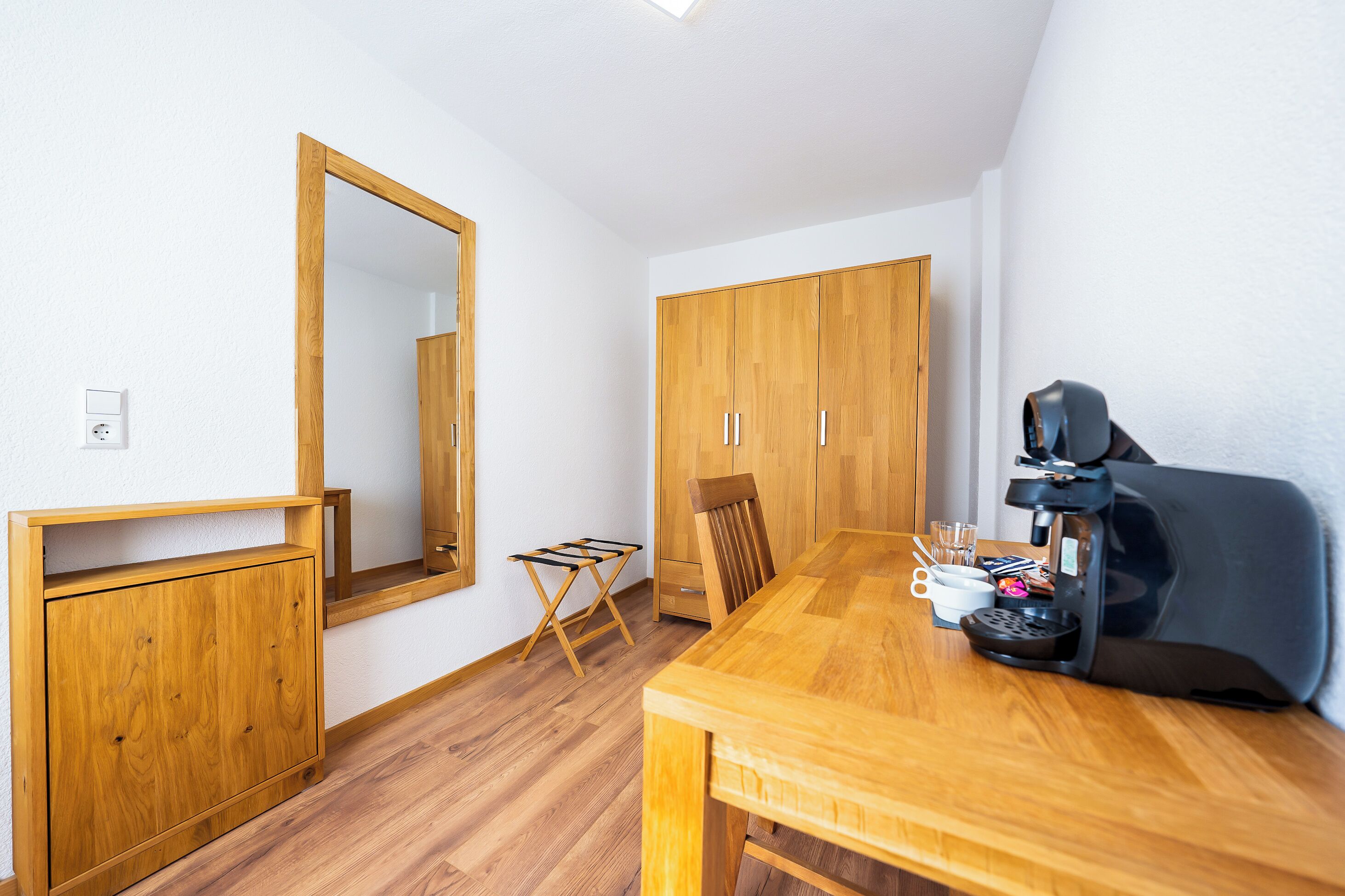 Una habitación compacta con una mesa de madera, una cafetera y un espejo en la pared.