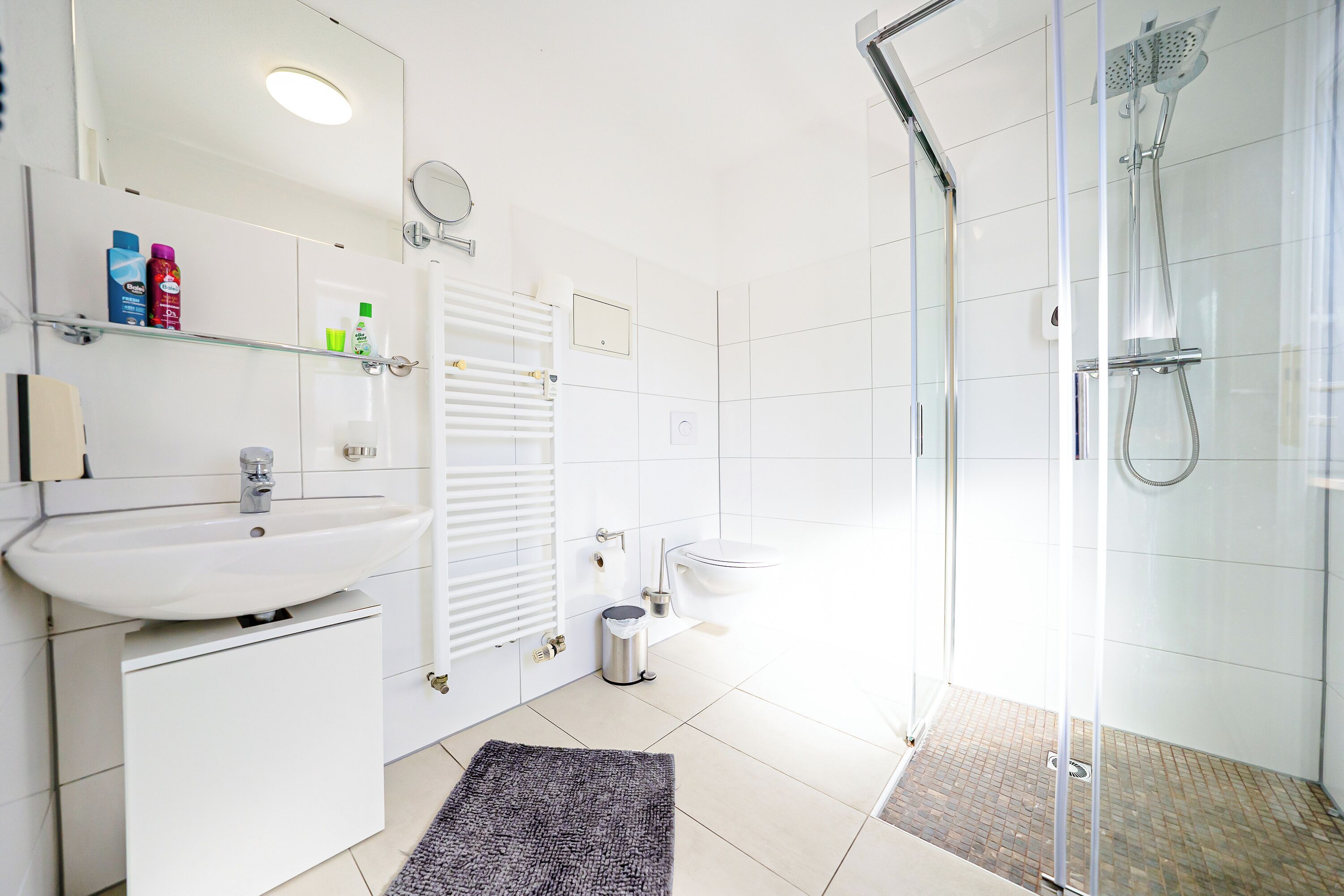 Un baño moderno con cabina de ducha de vidrio, lavamanos blanco y un inodoro.