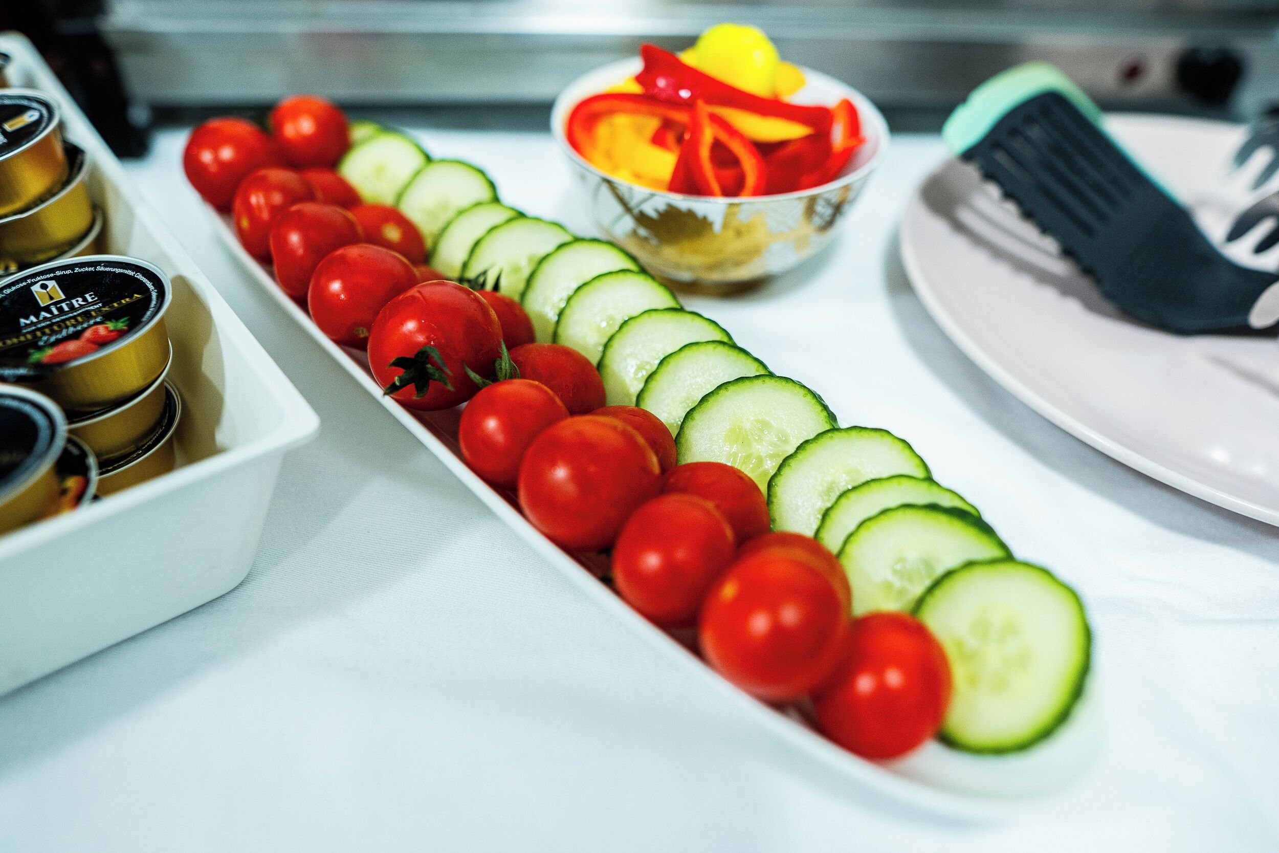 Un plateau de concombres et de tomates cerises coupés en tranches, un bol de poivrons coupés en lanières et une assiette avec une fourchette.