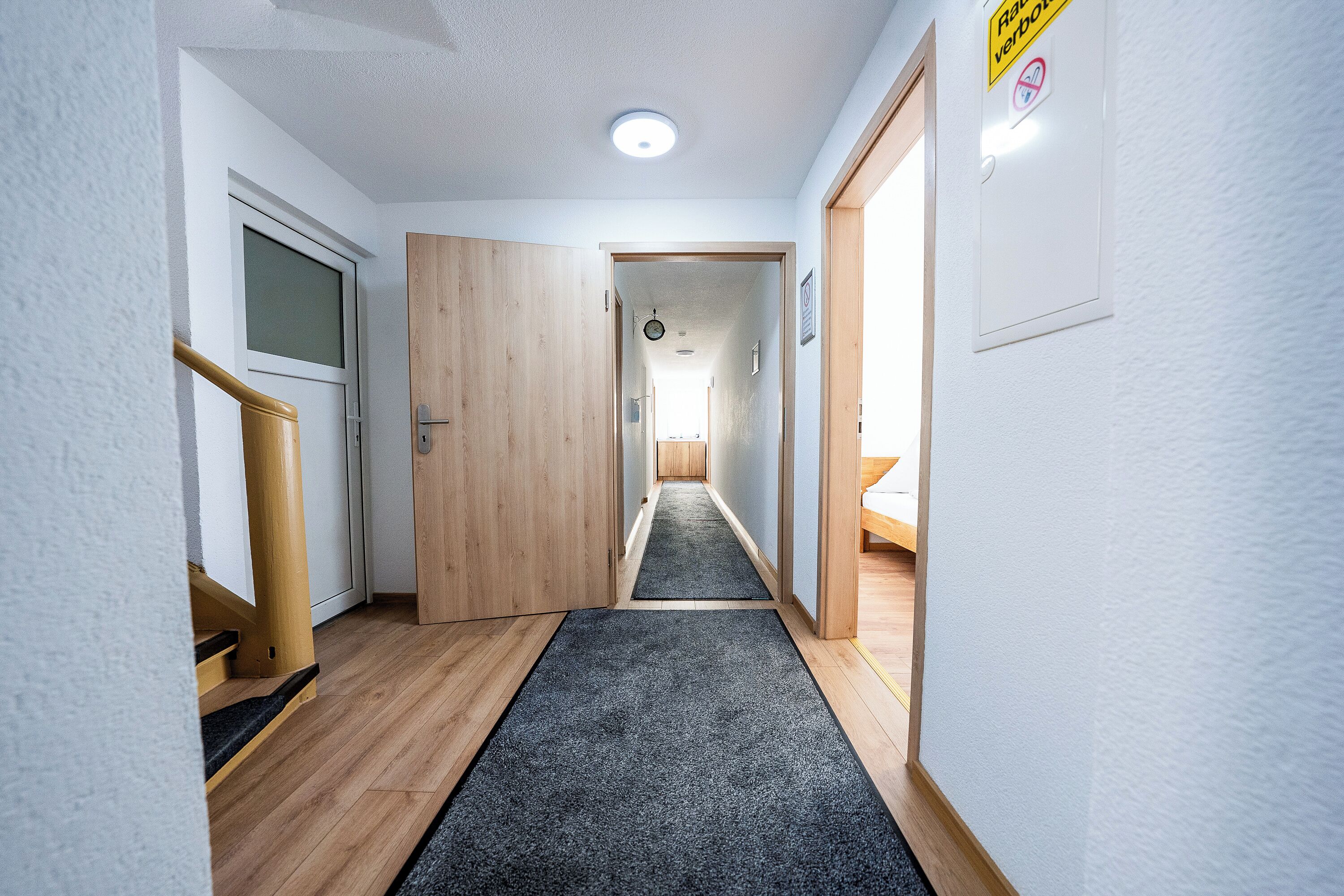 Un pasillo estrecho con piso de madera y una alfombra oscura que lleva a una puerta.