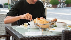 A person sitting at an outdoor table with a basket of bread, a cup, and a plate with food.