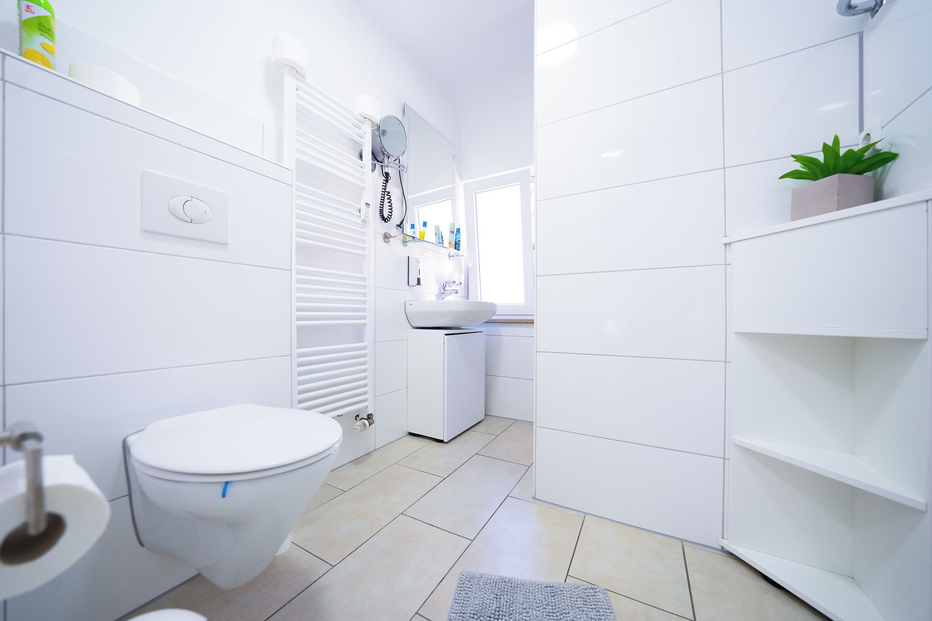 A modern bathroom with a toilet, sink, and a small shelf with toiletries.