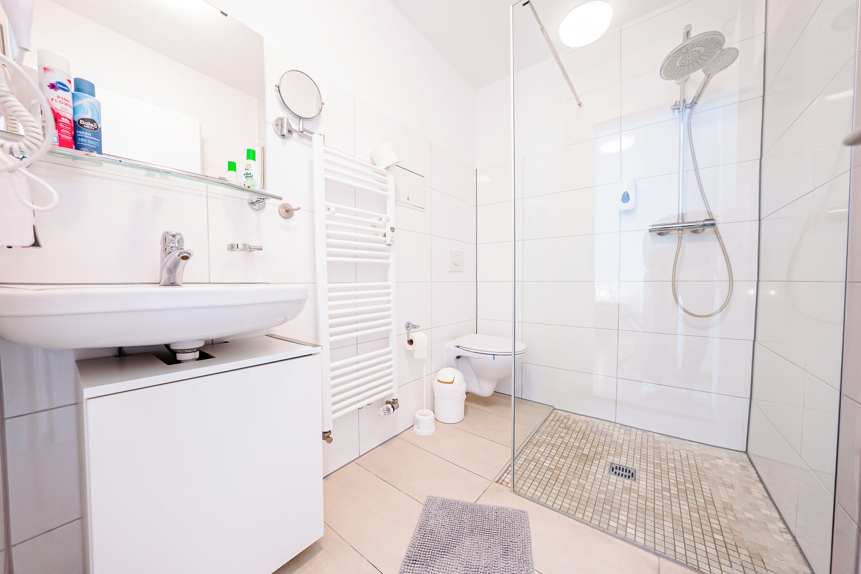 Un baño moderno con lavamanos blanco, espejo y cabina de ducha de vidrio.