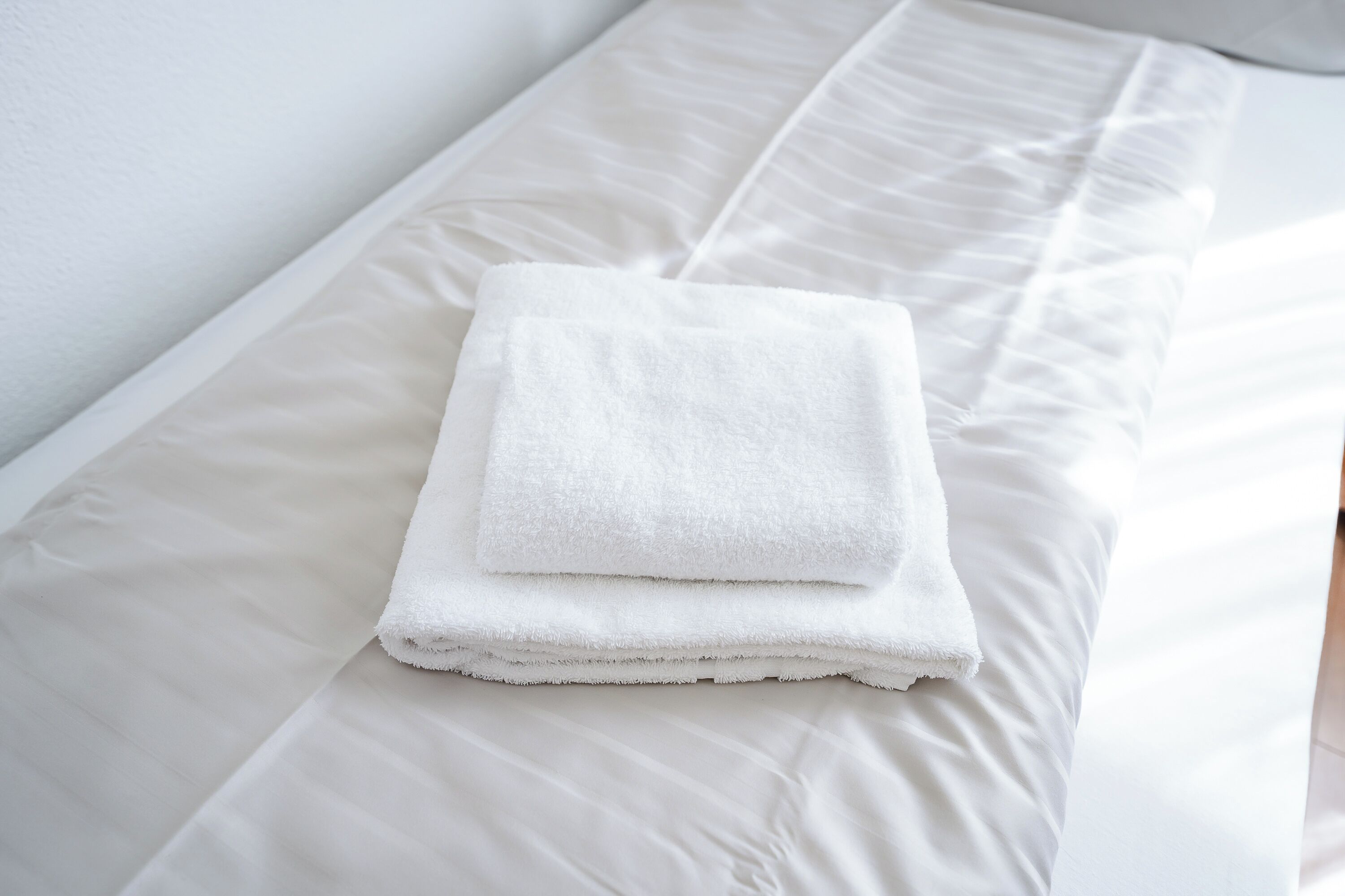 A neatly made bed with white linens and a folded white towel on top.