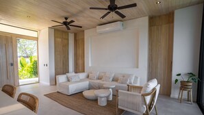Ein modernes Wohnzimmer mit einer Eckcouch, runden Couchtischen und einem Essbereich mit weißem Tisch und Korbstühlen.