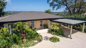 Ein modernes Haus mit Satteldach, einer überdachten Terrasse und einem Garten mit verschiedenen Pflanzen.