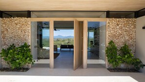 Ein moderner Eingangsbereich mit Steinwand und Glastüren, der auf eine Terrasse mit Bergblick führt.