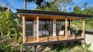 A modern outdoor living space with a wooden deck, glass walls, and a bed.
