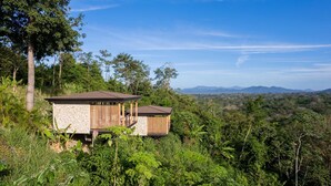 A secluded cabin with a stone exterior and wooden accents, surrounded by dense forest and overlooking a mountainous landscape. - Chic 1BR Escape Breathtaking Balcony Views (Cóbano)