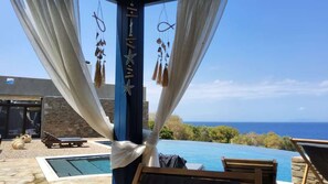 Un espace aménagé au bord de la piscine, avec vue sur la mer, un mur en pierre et un fauteuil de relaxation.
