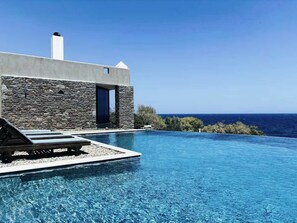 A modern villa with a stone facade, a swimming pool, and a view of the ocean. - Villa Scorpio - Infinity Pool Endless Blue Escape (Lavreotiki)