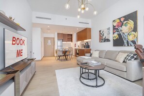 Ein modernes Wohnzimmer mit einer Couch, einem Couchtisch und einem an der Wand befestigten Fernseher mit dem Schriftzug 'BOOK ME'.
