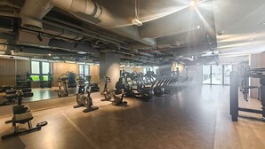 Un gimnasio amplio con diversas máquinas de cardio, estaciones de pesas y espejos.