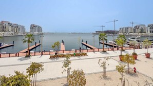 Un paseo marítimo con un puerto deportivo, palmeras y edificios modernos al fondo.