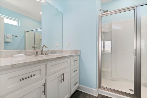 Une salle de bain dotée d’un comptoir en marbre, d’une douche à parois de verre et de meubles blancs.
