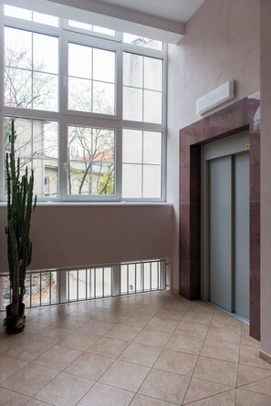 A spacious room with large windows, a potted plant, and an elevator.