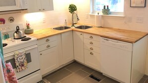 A kitchen with white cabinets, a wooden countertop, a stainless steel sink, a microwave, and a stove. - Charming 4BR Duplex Home |  5&6 (Kansas City)