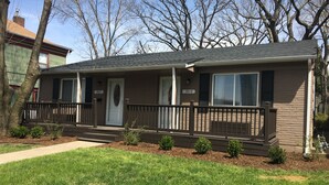 A two-story house with a front porch, a mailbox, and a small front yard with trimmed bushes. - Charming 4BR Duplex Home |  5&6 (Kansas City)