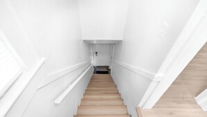 Eine schmale Treppe mit weißen Wänden und Holzstufen, die zu einer Tür oben führt.