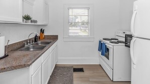 Eine kleine Küche mit weißen Schränken, einer Granit Arbeitsplatte, einem eingebauten Backofen und einem Fenster mit Jalousien.