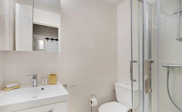 A modern bathroom with a white sink, mirror, and glass shower enclosure. - Lovely Studio in the Heart of the Marais (Paris)
