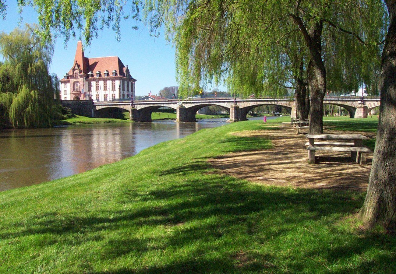 A riverside park with a historic building, a stone bridge, and a picnic area.
