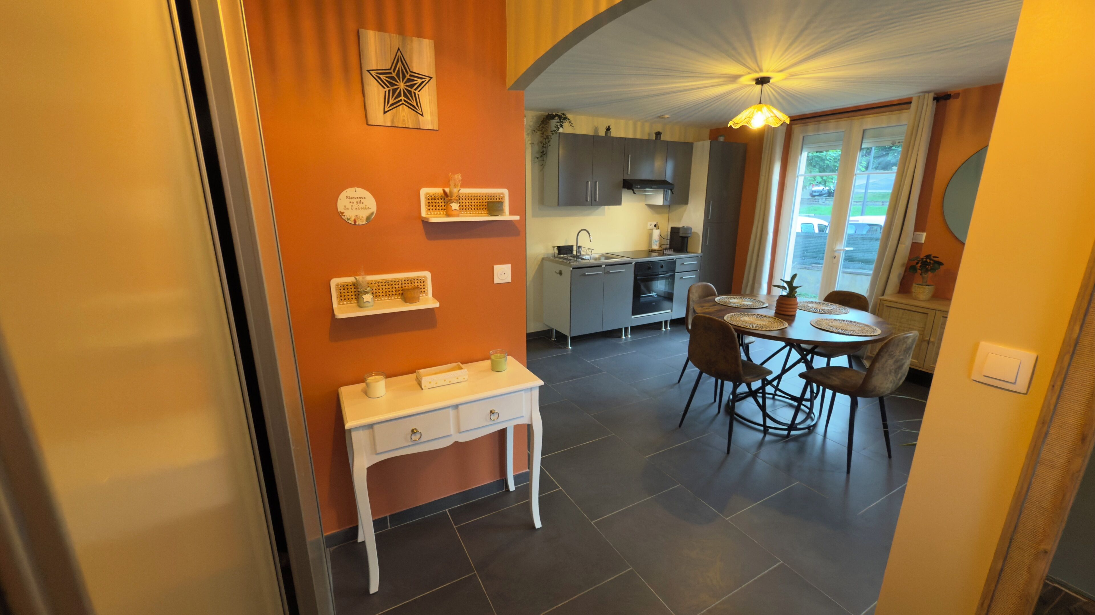 Een moderne keuken met grijze kastjes, een wit aanrechtblad en een eethoek met een ronde tafel en stoelen.