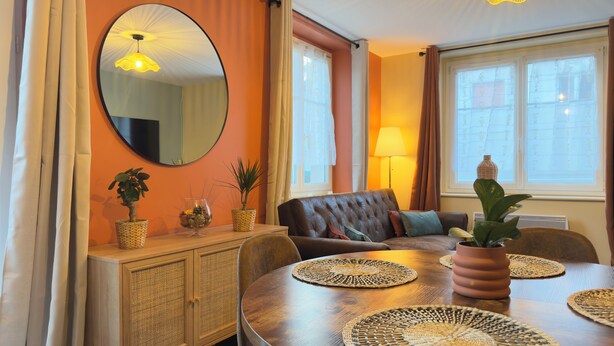 Et spiseområde med et rundt bord, vævede servietringe, et spejl og en sofa.