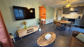 En moderne stue med et fladskærms-TV, et træ sofabord og et spiseområde med et rundt bord og stole.