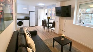 A compact living space with a sofa, a small table, a TV, a kitchen area, and a dining table with chairs. - Valdecanillas 1 bedroom (Madrid)