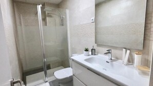 A modern bathroom with a glass-enclosed shower, a white toilet, and a vanity with a mirror. - Valdecanillas 1 bedroom (Madrid)