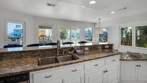 A modern kitchen with granite countertops, white cabinetry, and a large window offering a view of colorful buildings and palm trees.