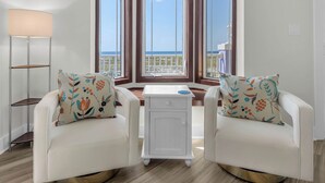 A room with two white armchairs, a small white side table, and a large window with a view of the sea.