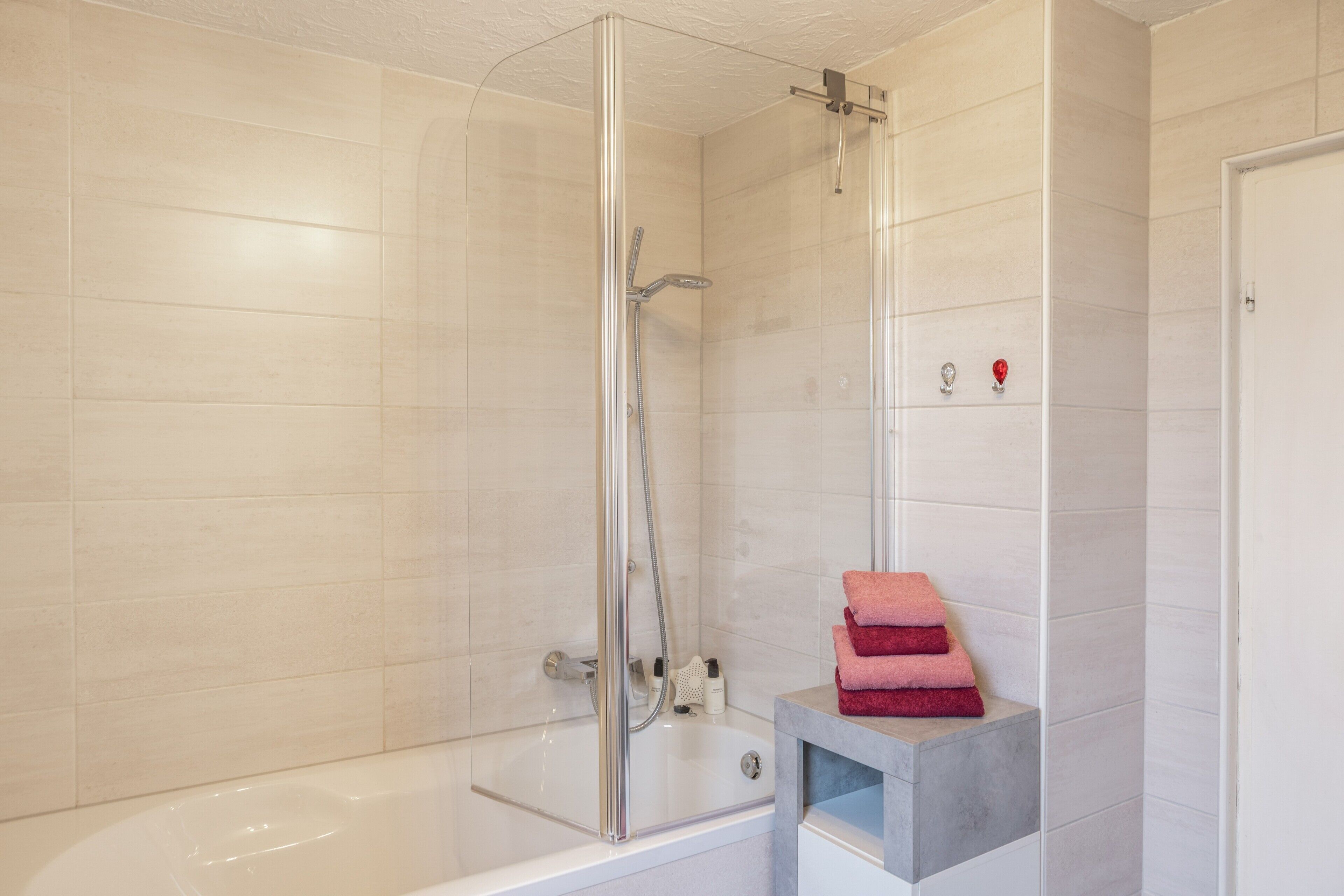 Ein modernes Badezimmer mit einer gläsernen Duschkabine, einer weißen Badewanne und einer kleinen Ablage mit Handtüchern.