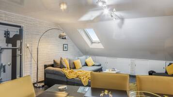Ein modernes Schlafzimmer im Loft-Stil mit schrägen Wänden, einem Oberlicht, einer Couch mit Kissen, einem Couchtisch und einem Schreibtisch mit einem Laptop.