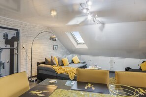 Un dormitorio estilo loft moderno con techo inclinado, tragaluces, un sofá con cojines, una mesa de centro y un escritorio con una computadora portátil.