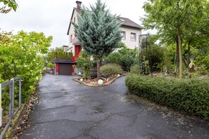 A residential driveway leading to a house with a red garage and a large coniferous tree in the center.