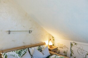 A bedroom with a sloped ceiling, a bed with a wooden headboard, a bedside lamp, and a wall with a bamboo plant mural.