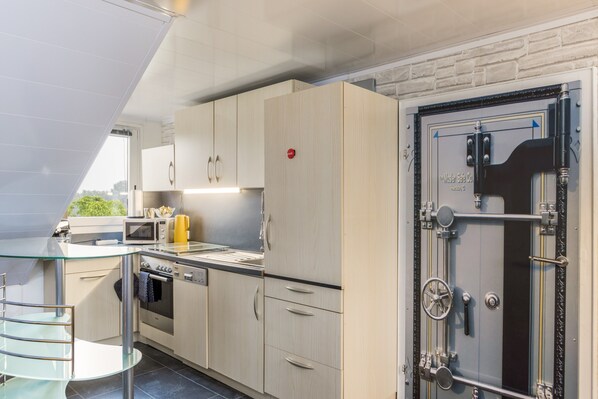 A modern kitchen with a glass-top dining table, stainless steel appliances, and a safe with a combination lock.