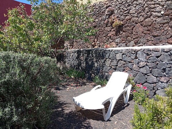 A white lounge chair in a garden area with a stone wall and various plants.