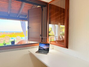 Un ordinateur portable est posé sur une table blanche près d’une fenêtre, d’où l’on peut voir une piscine et de la verdure.