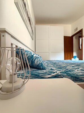A bedroom with a bed, a white wardrobe, and a wall-mounted light fixture.