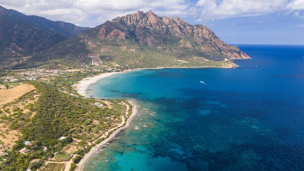 Ein Luftbild einer Küstenregion mit einem Berg, klarem blauen Meer und einer bebauten Uferlinie.