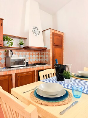 Une cuisine équipée d’un four à micro-ondes, d’une cuisinière et de placards, une table à manger avec des assiettes et des couverts, et une horloge au mur.