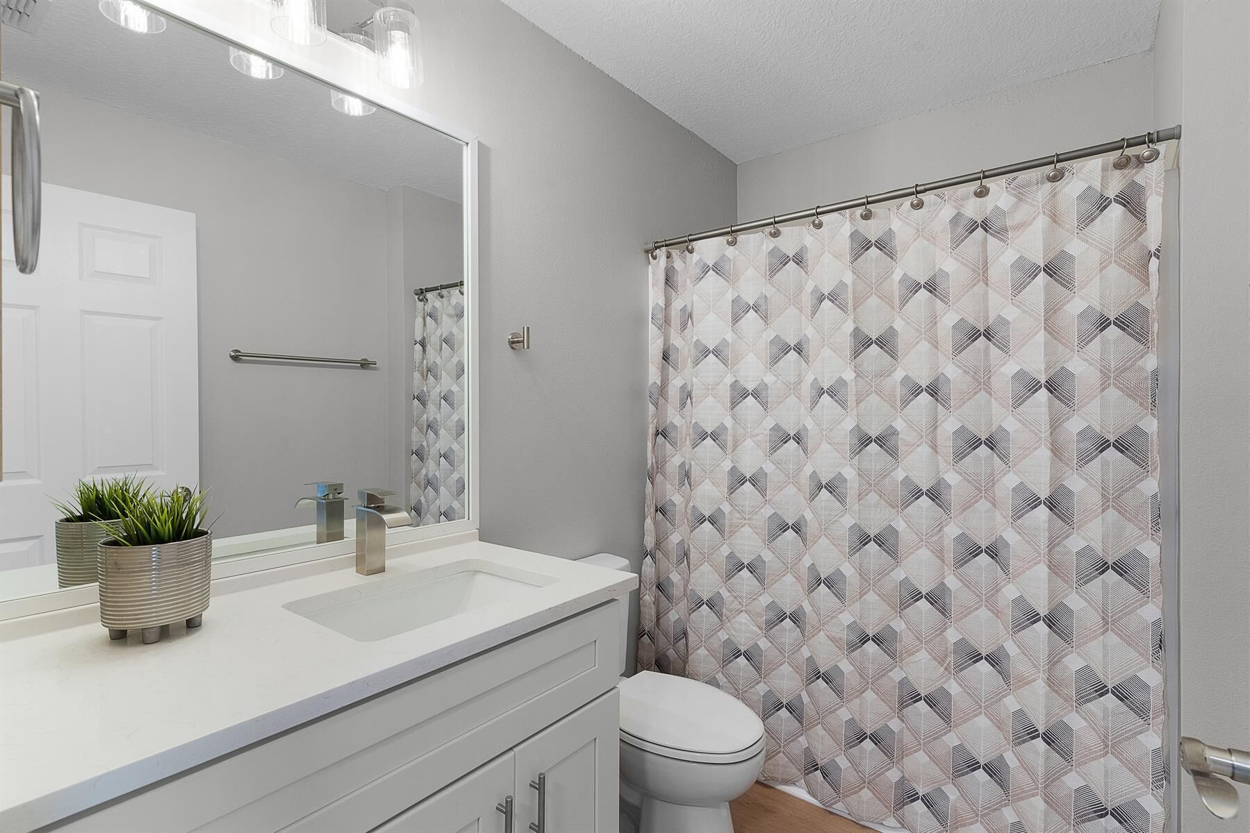 Une salle de bain avec un lavabo blanc, un miroir, des toilettes et un rideau de douche à motifs géométriques.