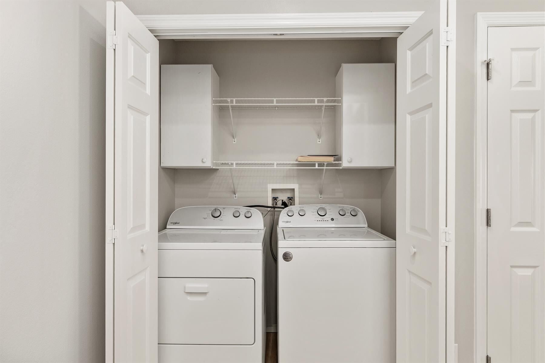A laundry room with two stacked washers and dryers, white cabinets above, and a small shelf with a book.