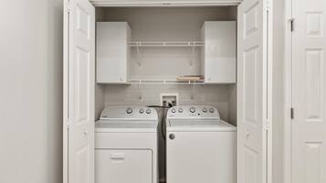 A laundry room with two stacked washers and dryers, white cabinets above, and a small shelf with a book.