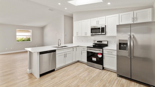 A modern kitchen with white cabinetry, stainless steel appliances, and a skylight.