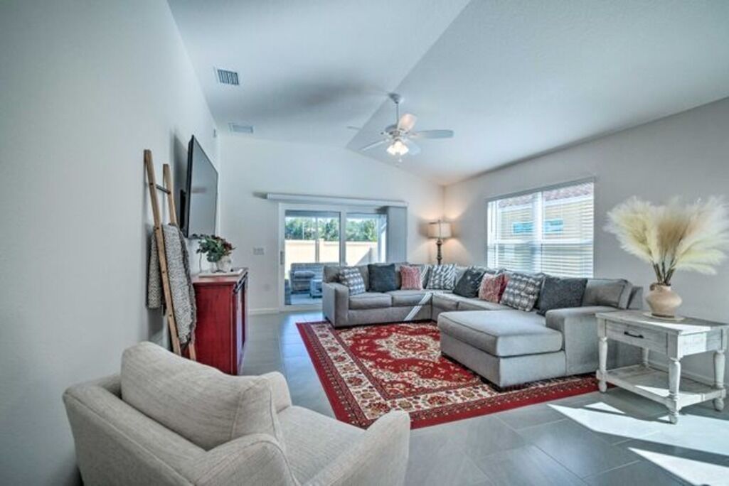 A spacious living room with a grey sofa, a red rug, and a ceiling fan.