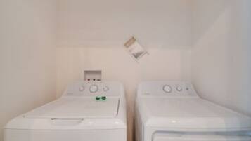 A laundry room with two white washing machines and a power outlet on the wall.